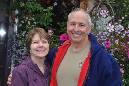 A smiling man and woman stand together in a garden at Alaska Adventure Cabins.