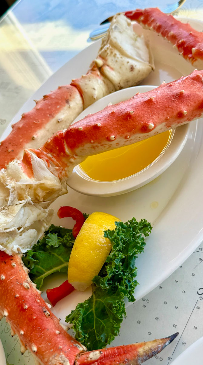 King crab legs served on a plate with melted butter, a lemon wedge, and kale, a classic highlight among things to do in Homer Alaska.