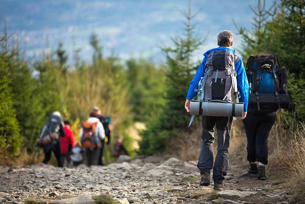 A group of hikers with backpacks walking up a rocky mountain trail, one of many things to do in Homer Alaska.